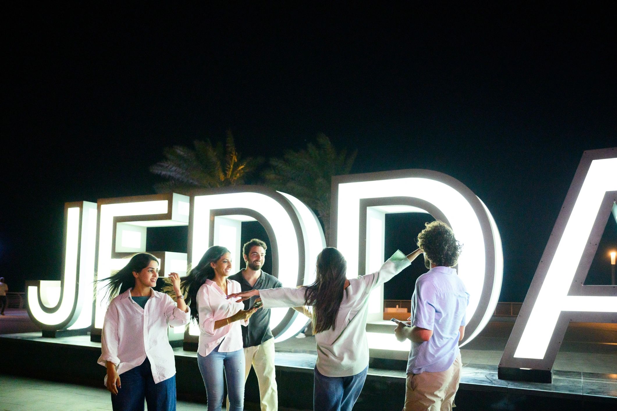 Friends celebrating outdoors at night near a lit sign