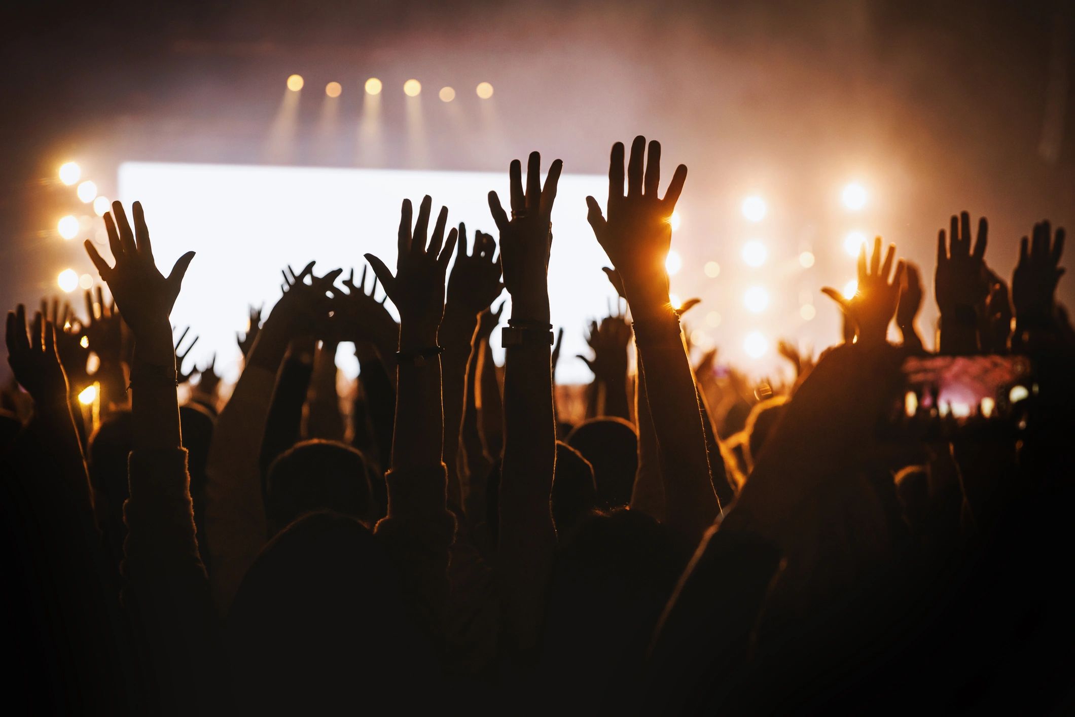 Audience with raised hands and phones facing a brightly lit stage